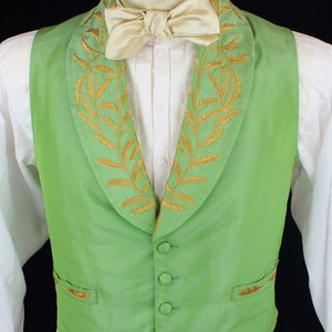 May include: A green vest with a gold embroidered floral pattern around the collar. The vest has five buttons and a pocket on the left side.