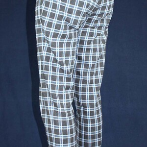 May include: Black and blue plaid pants with a white shirt and suspenders. The pants have a straight leg and are worn with black shoes.