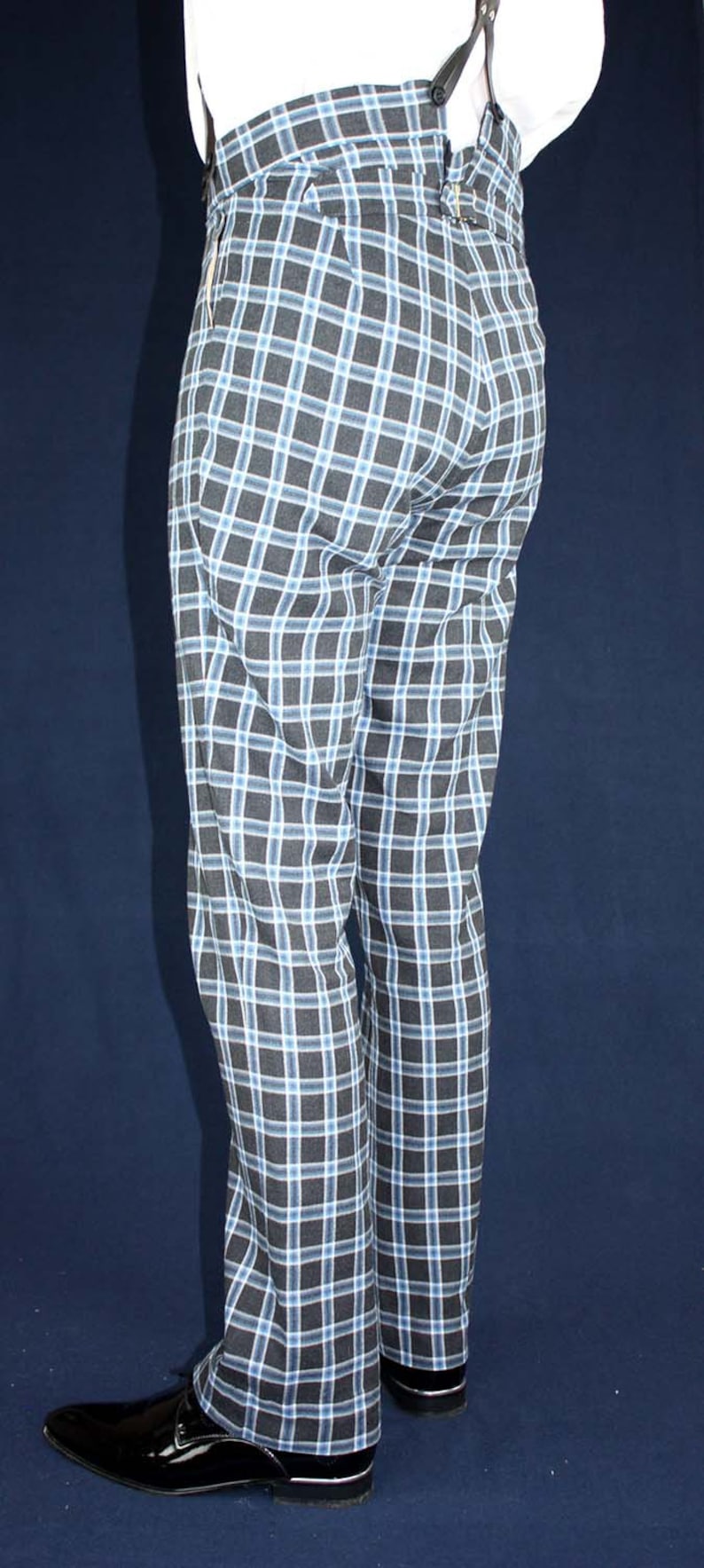 May include: Black and blue plaid pants with a white shirt and suspenders. The pants have a straight leg and are worn with black shoes.