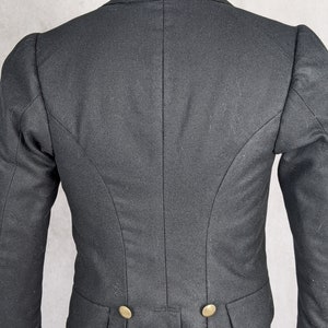 May include: Black tailcoat with a high collar and two gold buttons. The coat has a long, flowing back.