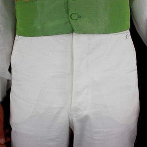 May include: A white pair of pants with a green vest. The vest has gold embroidery and four black buttons.