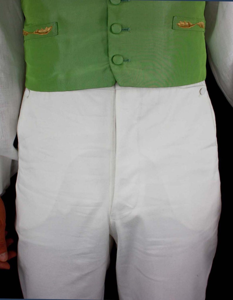 May include: A white pair of pants with a green vest. The vest has gold embroidery and four black buttons.