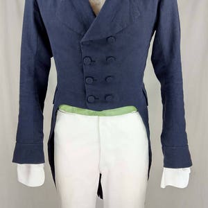 May include: A navy blue tailcoat with a double-breasted closure and five buttons. The tailcoat has a white shirt underneath with a cream-colored bow tie.