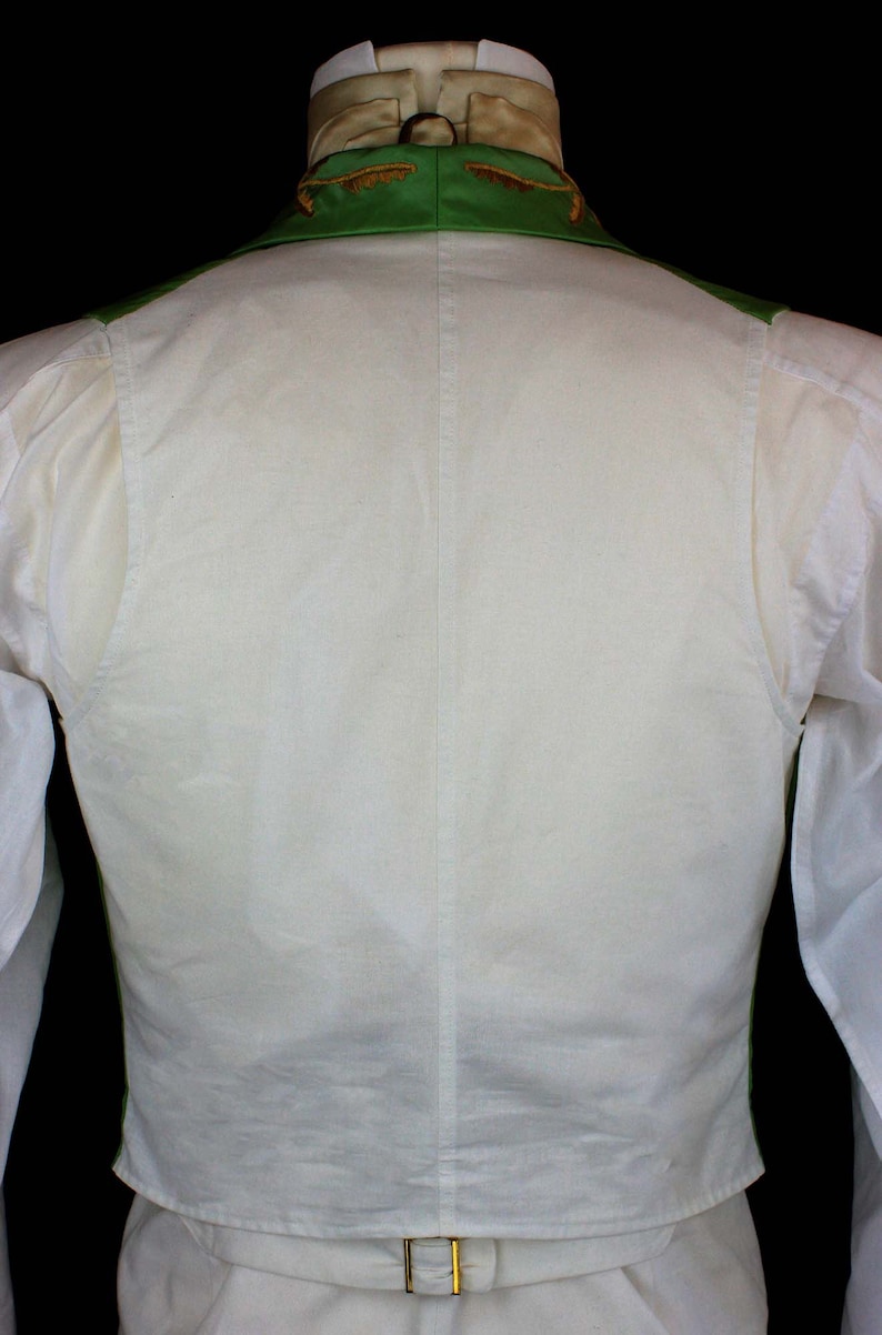 May include: A white vest with a green collar and gold trim. The vest is worn over a white shirt with a bow tie.