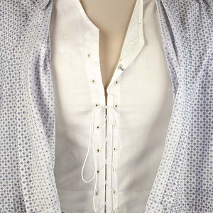 May include: A white shirt with a lace-up front and a white collar. The shirt is made of a lightweight fabric and has a relaxed fit.