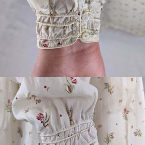 May include: Close-up of a white cotton blouse with a floral print. The blouse has a gathered elastic cuff at the wrist.