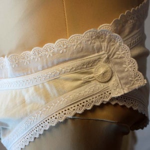 May include: White cotton undergarment with a lace trim and a button fastening. The garment features a delicate embroidered design.
