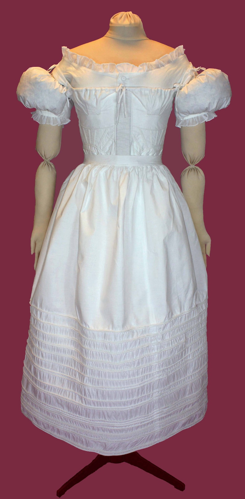 May include: A white cotton dress with a ruffled neckline and puffed sleeves. The dress has a fitted bodice and a full skirt with multiple layers of ruffles at the hem.