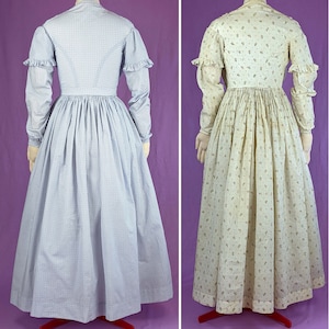 May include: Two vintage dresses, one in a light blue and white pattern and the other in a cream and brown floral pattern. Both dresses have long sleeves and a gathered skirt.