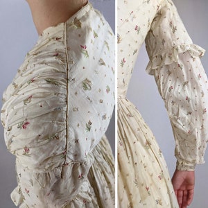 May include: A vintage white cotton dress with a floral print. The dress has a gathered bodice and long sleeves with ruffles at the cuffs.