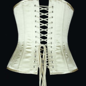 May include: A white satin corset with a lace-up back. The corset has a long, white ribbon tie at the bottom.