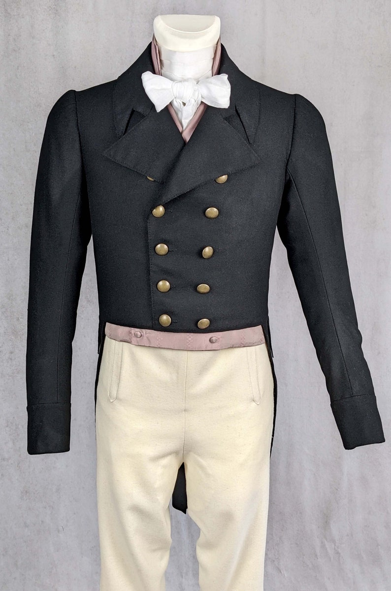 May include: A black tailcoat with gold buttons and a white bow tie. The tailcoat is worn over a white shirt and a pink vest. The person is wearing white pants.