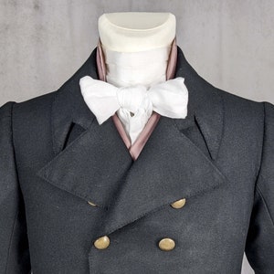 May include: A black double-breasted jacket with gold buttons and a white bow tie with a pink lining.