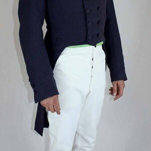 May include: A man wearing a dark blue tailcoat with a white cravat and white pants. He is wearing black shoes and glasses.