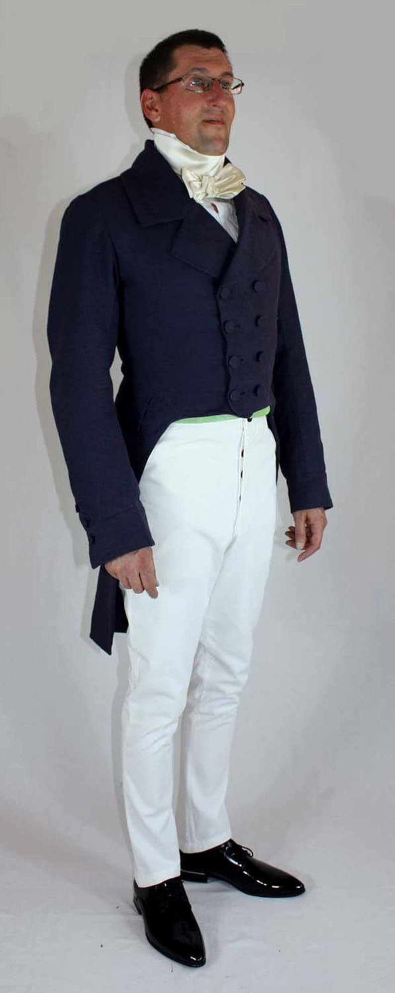 May include: A man wearing a dark blue tailcoat with a white cravat and white pants. He is wearing black shoes and glasses.