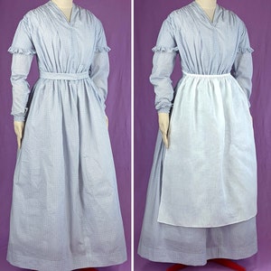 May include: A blue and white patterned dress with a white apron. The dress has a v-neck and long sleeves with ruffles at the cuffs. The apron is tied at the waist and hangs to the floor.