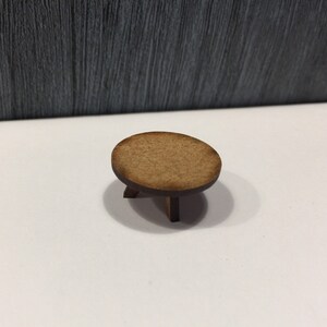 May include: A small, round wooden table with three legs. The table is made of light brown wood and has a smooth, polished finish.