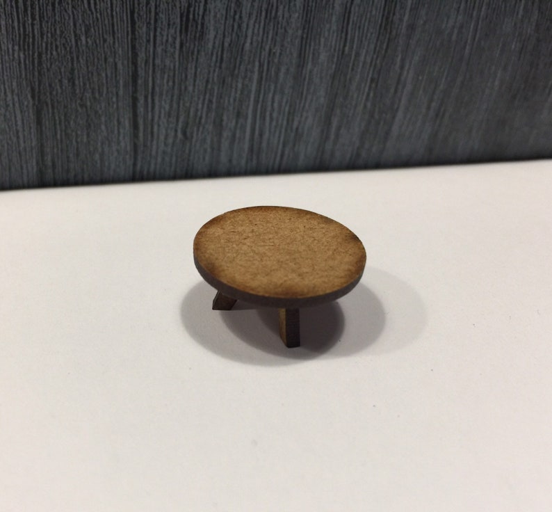 May include: A small, round wooden table with three legs. The table is made of light brown wood and has a smooth, polished finish.