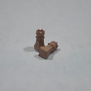 May include: Two brown chess rook pieces. One rook is upright, and the other is lying on its side. The rooks have a crown-like top and a square base. The pieces are made of a clay-like material.