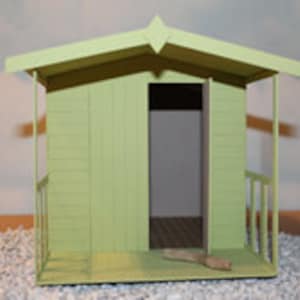 May include: A light green wooden shed with a small porch and a door. The shed has a peaked roof and is surrounded by small white rocks.
