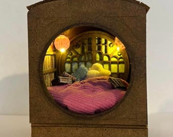 May include: A wooden miniature bedroom scene with a pink bed, a window with stained glass, and a small lamp. The scene is lit from within, creating a warm glow.