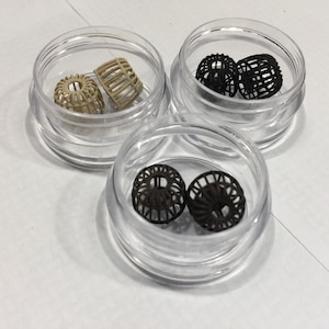 May include: Three small clear plastic containers each holding two small, round, decorative, wire mesh ornaments. One container holds two beige ornaments, one holds two black ornaments, and the other holds two dark brown ornaments.