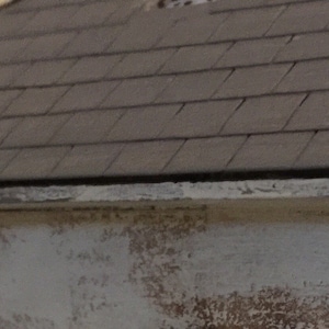 Op de afbeelding: Een verweerd, wit geverfd gebouw met een grijs dak van shingles. Het gebouw heeft een eenvoudig ontwerp met een rechthoekige vorm en een licht hellend dak.