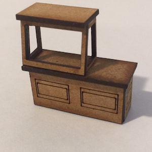 Puede incluir: Un mostrador de madera en miniatura con una vitrina en la parte superior. El mostrador es marrón con ribetes negros y tiene dos estantes. La vitrina está abierta en la parte delantera y tiene un panel de vidrio transparente.