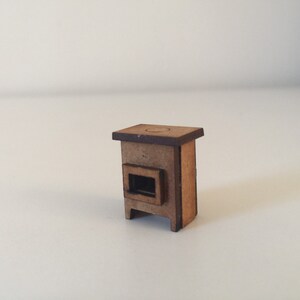 Puede incluir: Una estufa de madera en miniatura con un acabado marrón y una puerta negra. La estufa tiene una pequeña abertura en la parte superior para una chimenea.