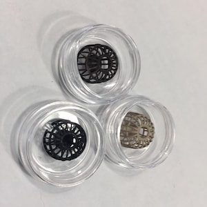 May include: Three small, round, clear plastic containers with lids. Each container holds a black, brown, and beige 3D printed object that resembles a small, intricate cage.