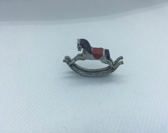 May include: A small, white rocking horse with a black mane and tail. The horse has a red saddle and is on a rocking base.