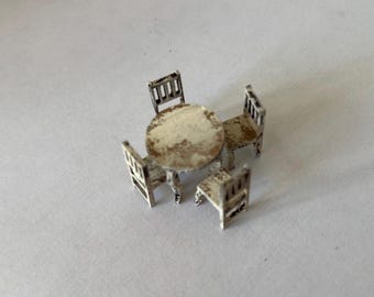 May include: Miniature dollhouse furniture set featuring a round table and three chairs. The set is painted in a distressed white finish, with visible wear and tear. The table and chairs are small, suitable for a dollhouse or similar display.