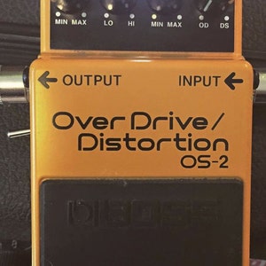 Op de afbeelding: Oranje Boss OS-2 Over Drive/Distortion gitaar effectpedaal met knoppen voor level, toon en drive. Het pedaal heeft een controlelampje dat aan staat.