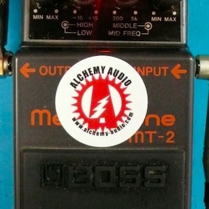 May include: A black Boss MT-2 Metal Zone guitar effects pedal with a red LED light on the top. The pedal has knobs for level, equalizer, and distortion. The pedal also has a sticker on the front that says "Alchemy Audio".