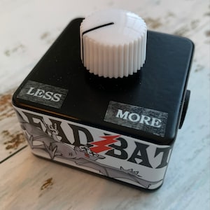 May include: Black guitar effects pedal with a white knob and a sticker of a bat with the words "Bad Bat" on it. The pedal has labels that say "Less" and "More".