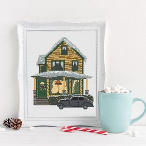 May include: A cross-stitch pattern of a yellow house with a green roof and white trim. The house is covered in snow and has a black car parked in front of it. The house has a porch with a wreath on the door and a Christmas tree in the window.