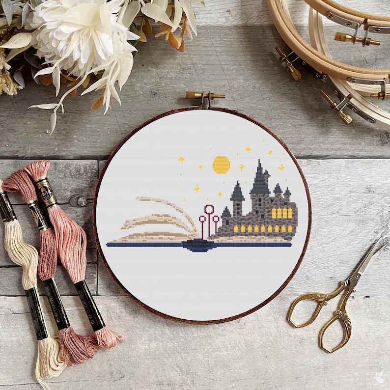 May include: A cross-stitch pattern of Hogwarts castle emerging from a book with a yellow moon and stars in the sky.