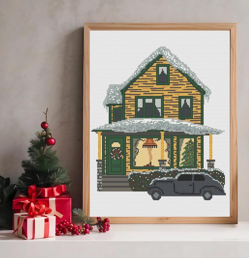 May include: A cross-stitch pattern of a yellow house with a green door and a black car in front of it. The house has snow on the roof and a wreath on the door. There is a Christmas tree in the window and a lamp with a leg lamp in the window.
