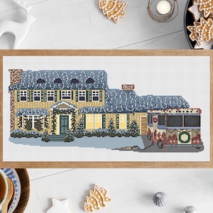 May include: A cross-stitch pattern of a yellow house with a blue roof and a red and white bus with a wreath on the side. The house is decorated with Christmas lights and a wreath on the door. The bus is decorated with Christmas lights and a wreath on the front. The scene is set against a white background.