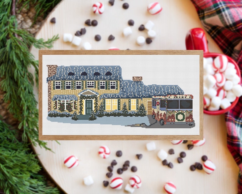 May include: A cross-stitch pattern of a yellow house with a red and green bus in front of it. The house has a white roof and is decorated with Christmas lights. The bus is decorated with a wreath and Christmas lights.