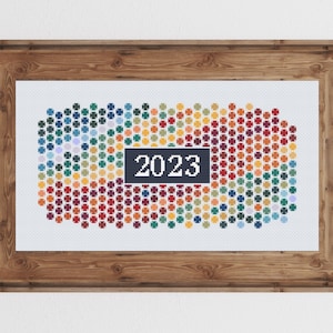 Op de afbeelding: Een ingelijst kruissteekontwerp met een kleurrijk abstract patroon van cirkels met het jaar 2023 in het midden.