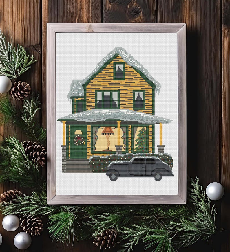 May include: A cross-stitch pattern of a yellow house with a green door and porch, covered in snow, with a black car parked in front. The house has a lit lamp in the window and a Christmas tree inside.