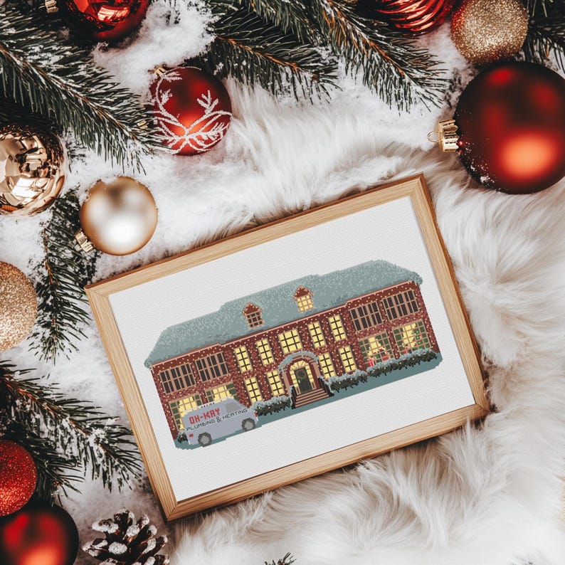 Puede incluir: Un patr&oacute;n de punto de cruz enmarcado de una casa cubierta de nieve con luces navide&ntilde;as. La casa tiene un exterior de ladrillo rojo y una puerta blanca. Una camioneta blanca con las palabras "Oh-Kay Plumbing & Heating" est&aacute; estacionada frente a la casa.