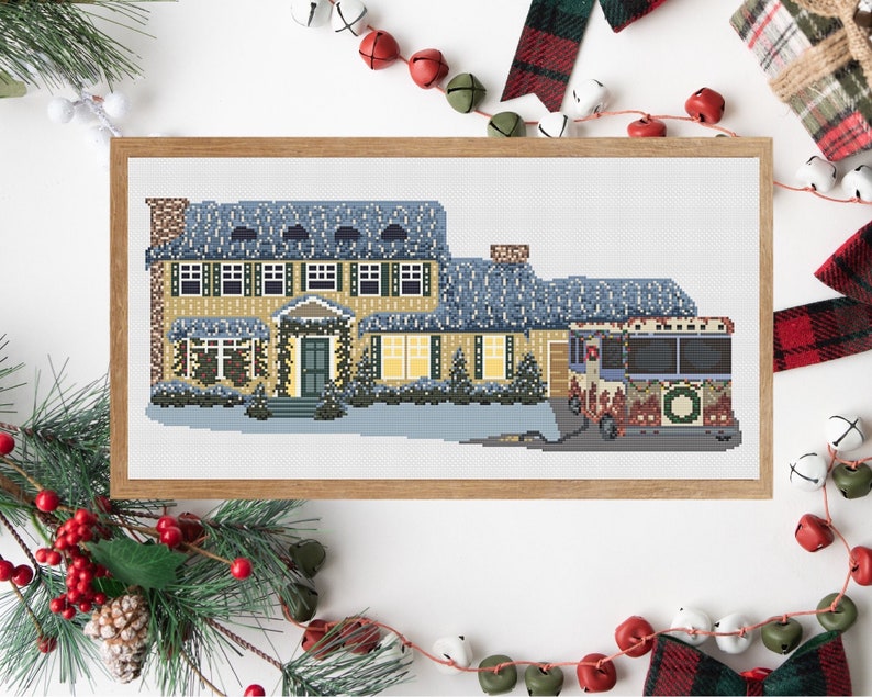 May include: A cross-stitch pattern of a yellow house with a blue roof and a snow-covered lawn. A red and white Christmas bus is parked in front of the house.