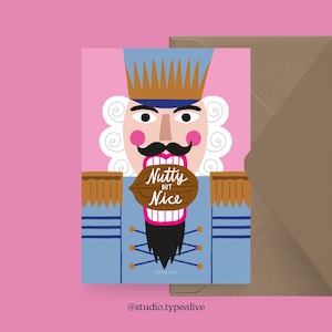 Op de afbeelding: Een wenskaart met een cartoon notenkraker ontwerp. De notenkraker draagt een blauw uniform met gouden details en een zwarte snor. Hij houdt een walnoot vast met de tekst "Nutty but Nice". De achtergrond is roze en een bruine envelop is inbegrepen.