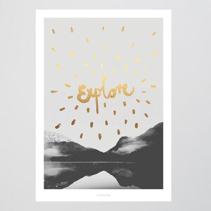 Könnte beinhalten: Ein Schwarzweißfoto eines Bergsees mit einer Spiegelung der Berge im Wasser. Das Wort "Explore" ist in Gold über den Bergen geschrieben.