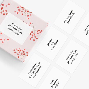 May include: A set of six white cards with black text, featuring humorous Christmas-themed phrases. The cards are arranged on a pink background with a red berry pattern.