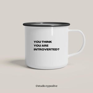 Könnte beinhalten: Weißer Emaille-Becher mit schwarzem Rand und Henkel. Der Becher trägt den Text "YOU THINK YOU ARE INTROVERTED?" in Schwarz, zentriert auf der Vorderseite. Der Becher steht vor einem neutralen Hintergrund.