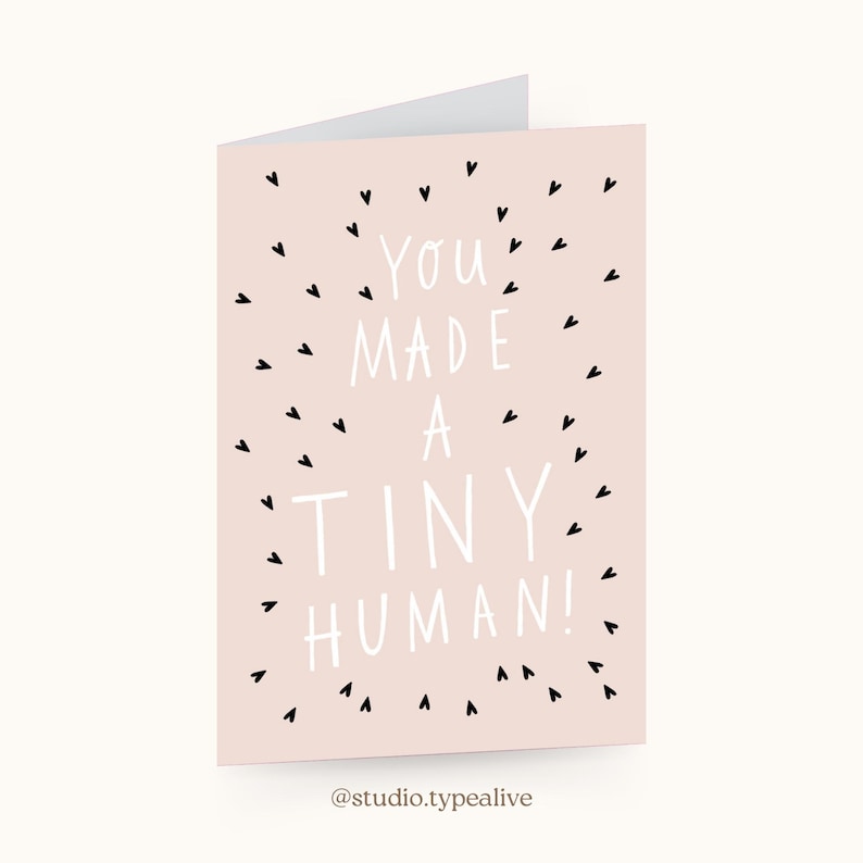 May include: A pink card with black hearts and white text that reads "You made a tiny human!"  The card is for a new parent.