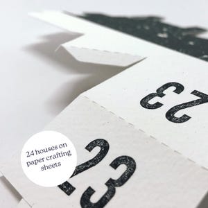 May include: Close-up of a paper craft advent calendar with the numbers 23 and 22 visible. The text "24 houses on paper crafting sheets" is visible in a circle.